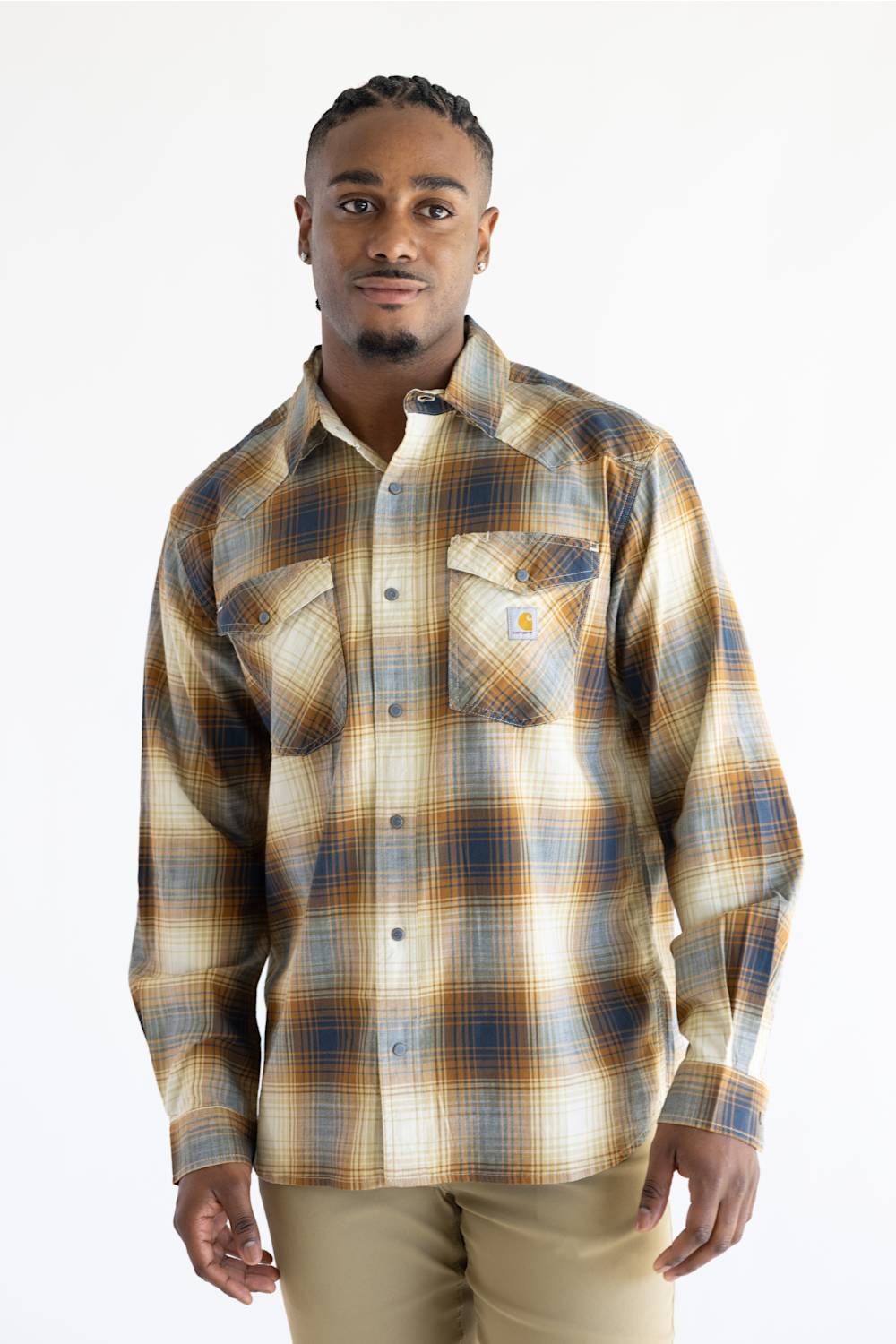 A man wearing a Carhartt long-sleeve plaid button-up shirt in beige, brown, and blue tones, paired with khaki pants, photographed against a plain white studio background.