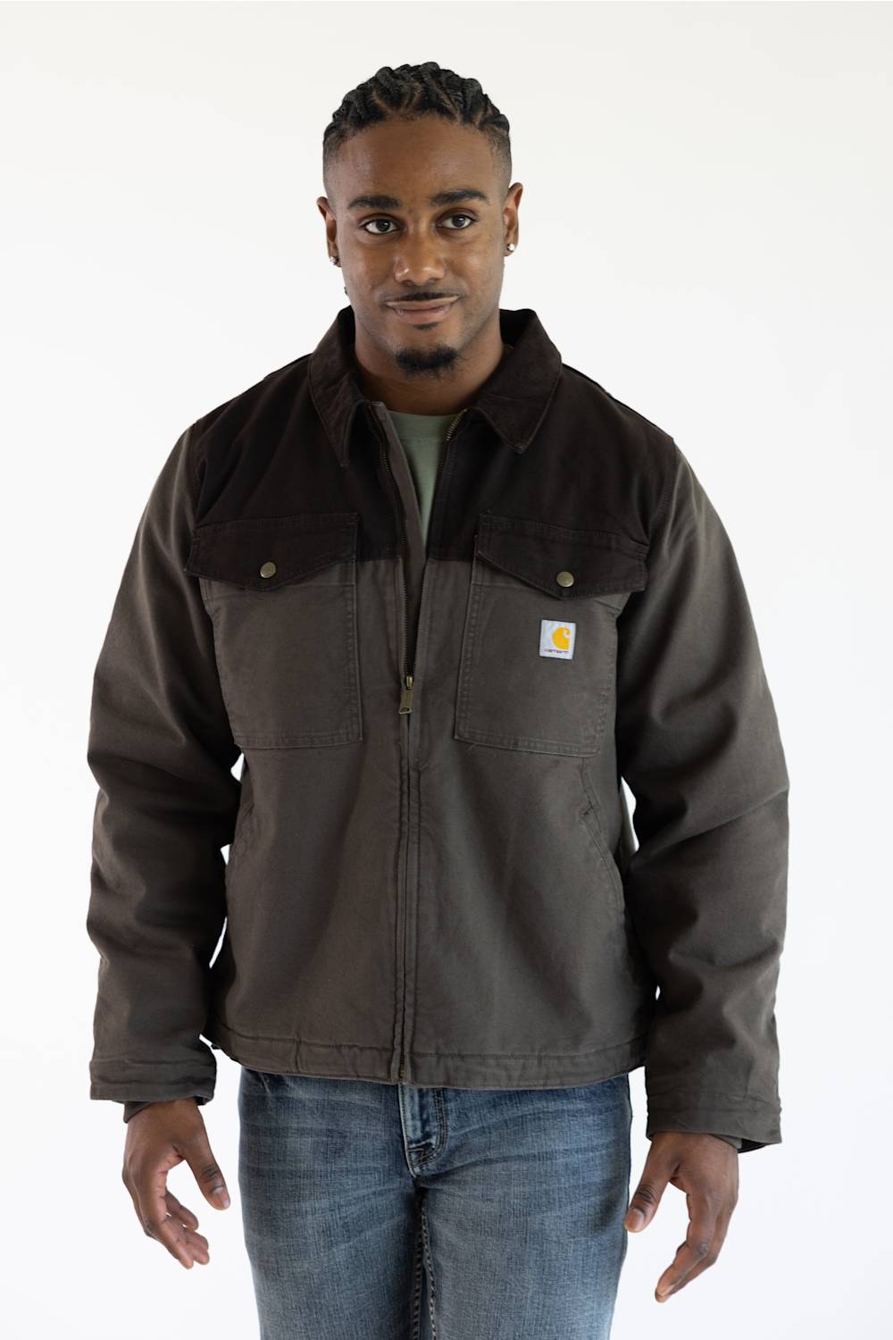 A man in a brown jacket and jeans stands against a plain white background.