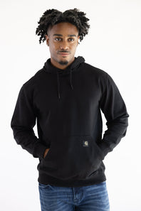 A man wearing a black Carhartt hoodie with a small brand patch on the front pocket, paired with blue jeans, against a plain white background.