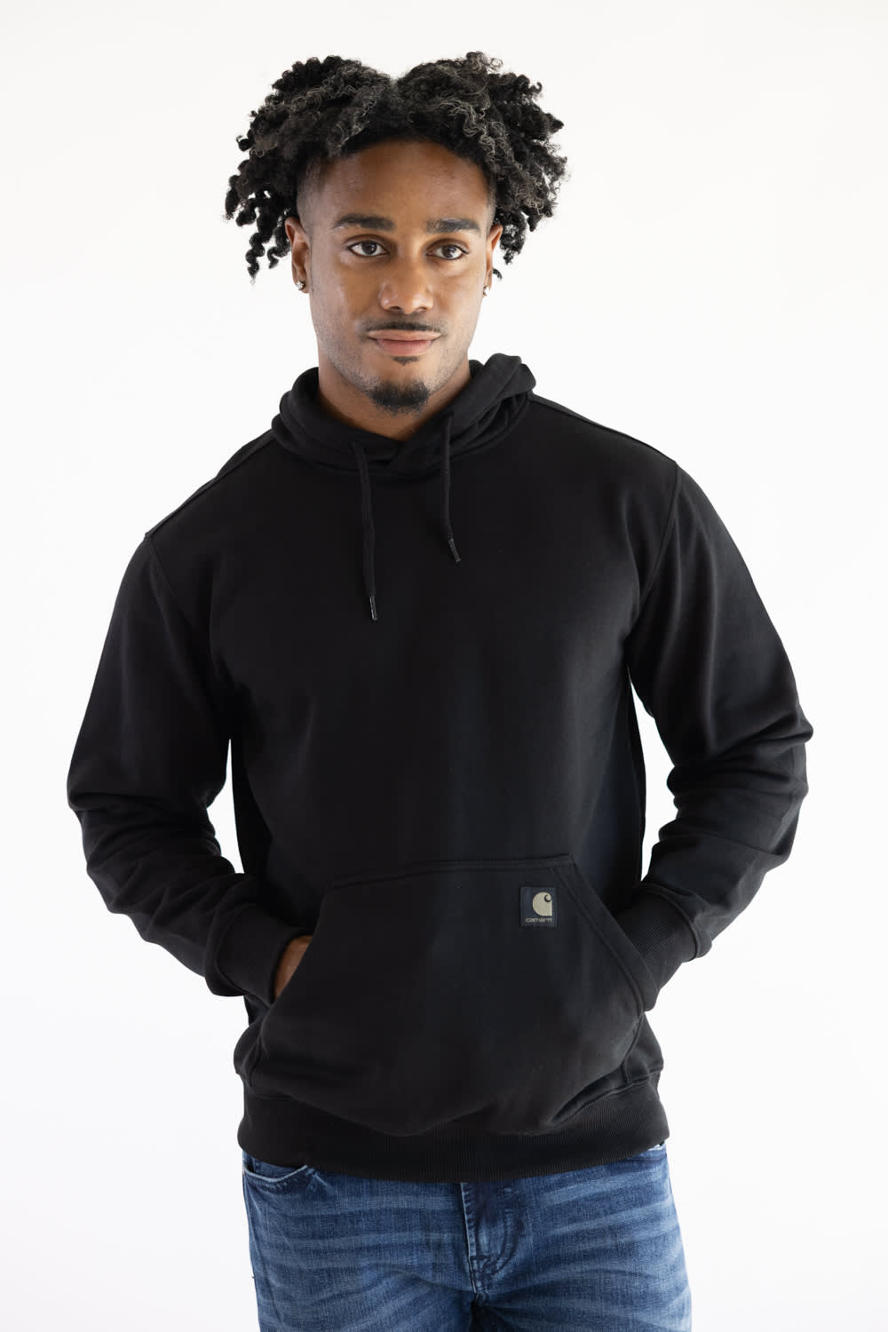 A man wearing a black Carhartt hoodie with a small brand patch on the front pocket, paired with blue jeans, against a plain white background.