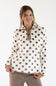 A smiling woman wearing a cream fleece pullover with brown polka dots and a brown zipper, paired with brown corduroy pants, against a plain white studio background.