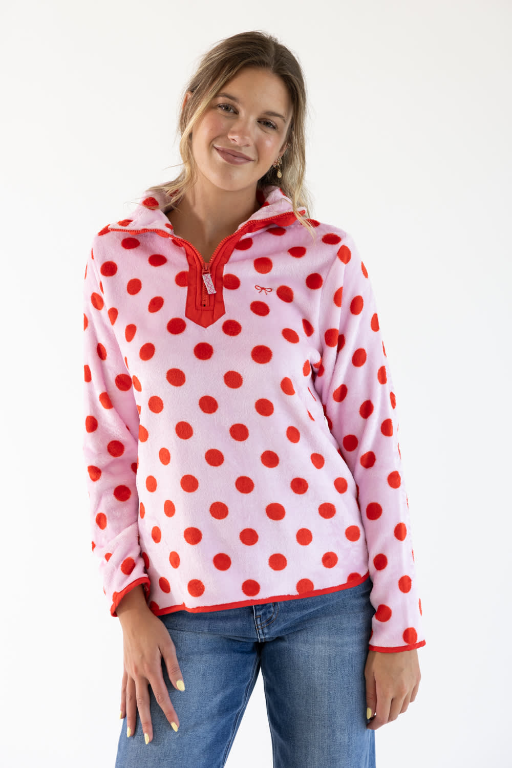 A woman wearing a pink fleece pullover with red polka dots and a red zipper, paired with blue jeans, against a plain white background.