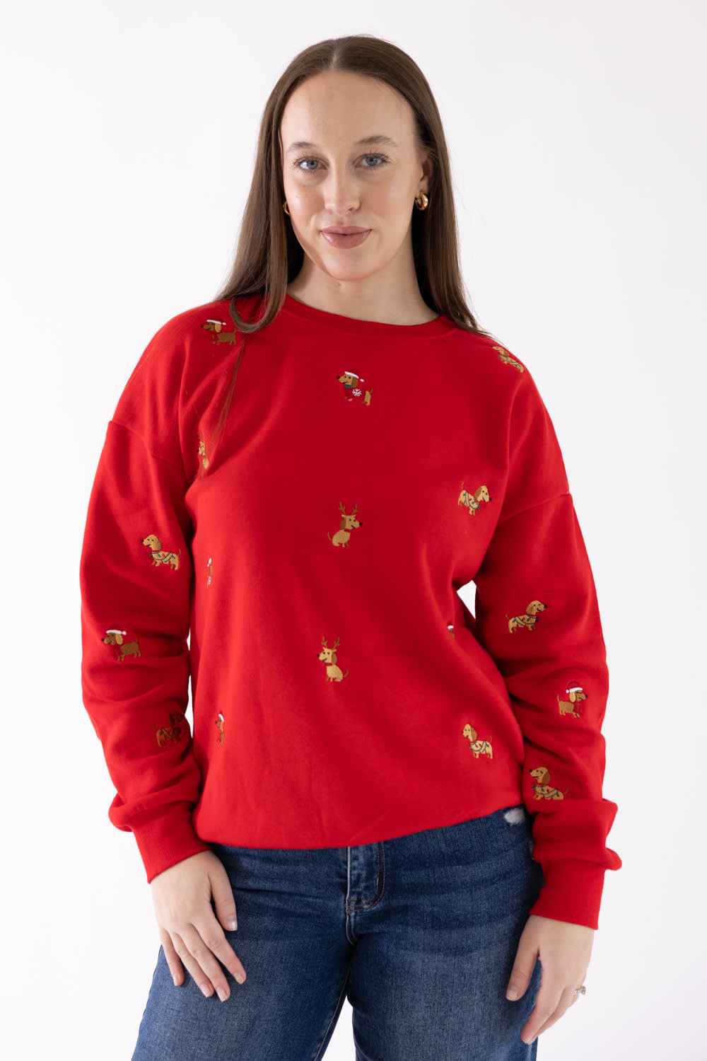 A woman wearing a bright red crewneck sweatshirt with small gold embroidered details, paired with blue jeans, against a plain white background.