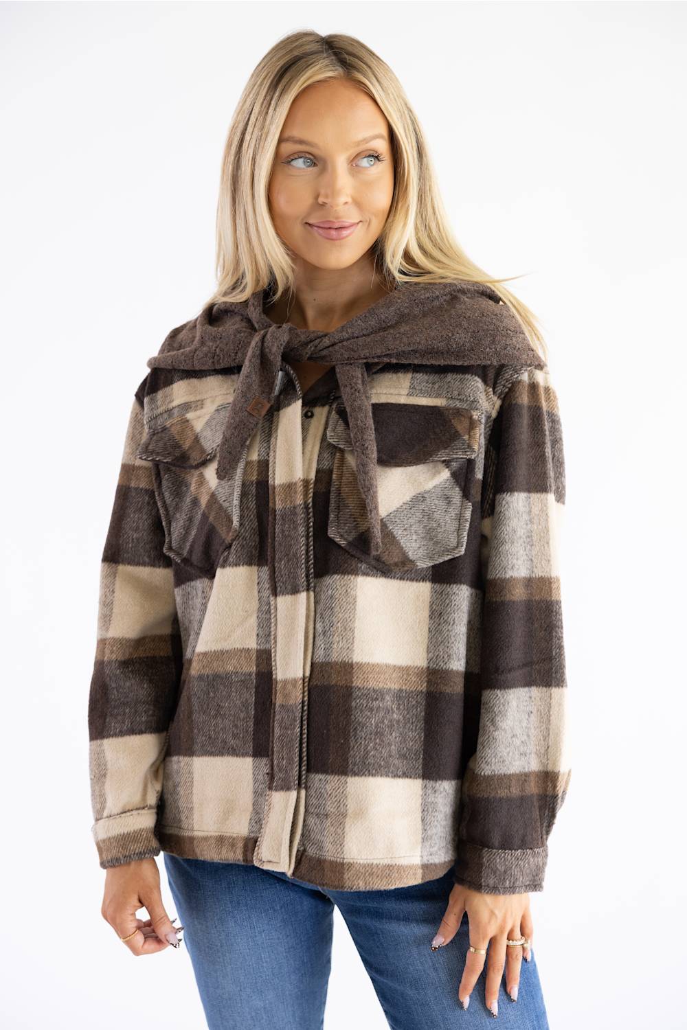 A woman wearing a brown and beige plaid hooded jacket with a tie-neck detail, paired with blue jeans, against a plain white background.