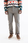 A person wearing slim-fit gray trousers, a multicolor patterned sweater, and brown shoes, shown from the chest down against a plain white studio background.