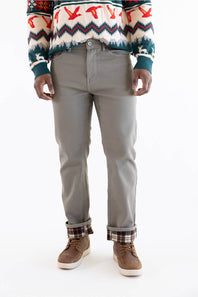 A person wearing slim-fit gray trousers, a multicolor patterned sweater, and brown shoes, shown from the chest down against a plain white studio background.