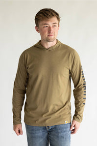 A man wearing a brown long-sleeve hooded shirt with a striped pattern on the right sleeve, paired with blue jeans, standing against a plain light gray background.