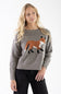 A woman wearing a heather gray knit sweater with a knitted fox motif in brown, white, and black, paired with black pants, against a plain white studio background.