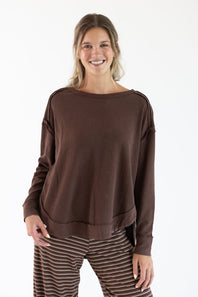 A woman modeling a brown long-sleeve knit top with a wide boat neckline and relaxed fit, paired with brown and white striped pants, against a plain white studio background.