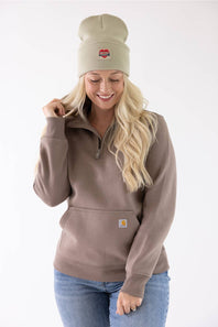 Woman wearing a faded olive green Carhartt watch cap beanie with a red heart logo patch and a brown half-zip sweatshirt.