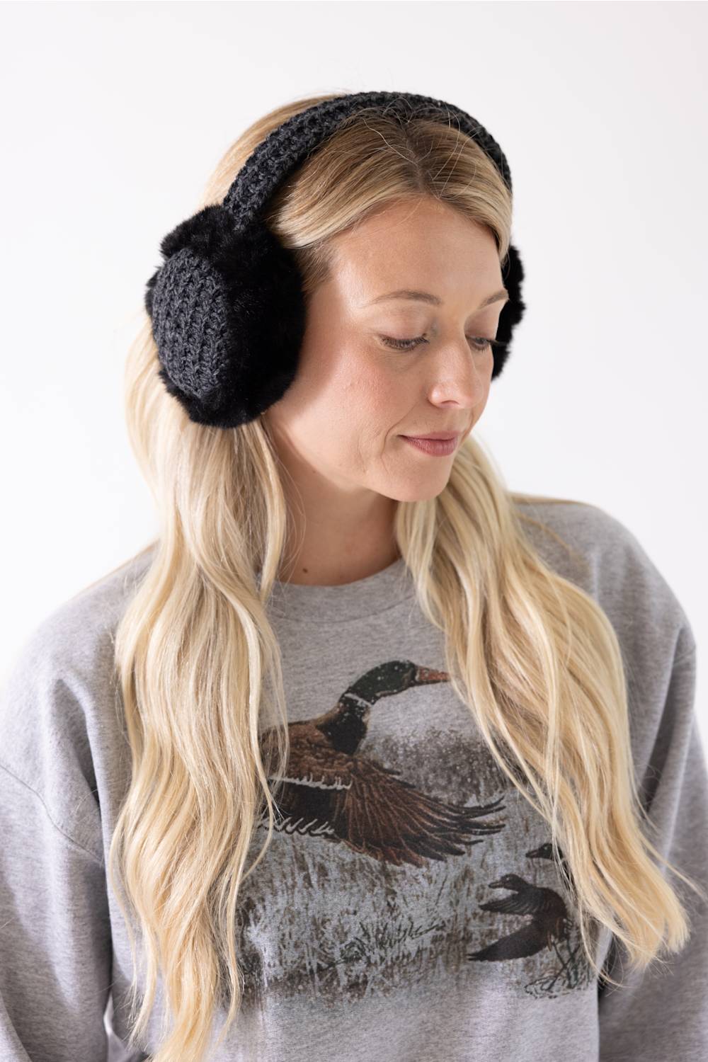 A woman with long blonde hair wearing charcoal grey C.C. heather knit earmuffs with black faux fur and a grey sweatshirt.