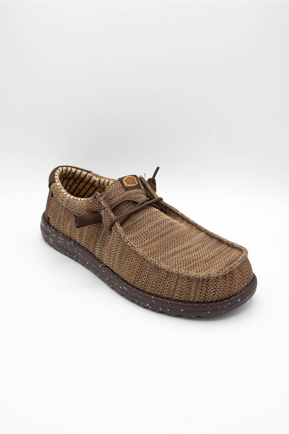 A single brown woven slip-on shoe with a textured knit upper, matching laces, and a speckled dark brown sole, shown against a plain light gray background.