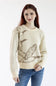 A woman with red hair wearing a cream-colored knit sweater with a brown graphic print of flying ducks, paired with blue jeans, against a plain white background.