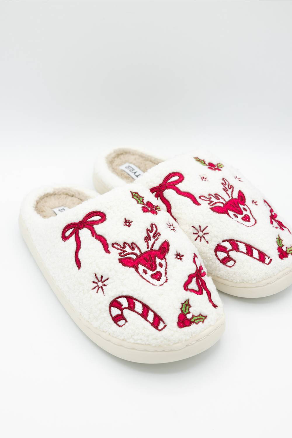 A pair of fuzzy white women's house slippers with embroidered festive holiday designs including a red reindeer, bow, candy canes, and snowflakes.