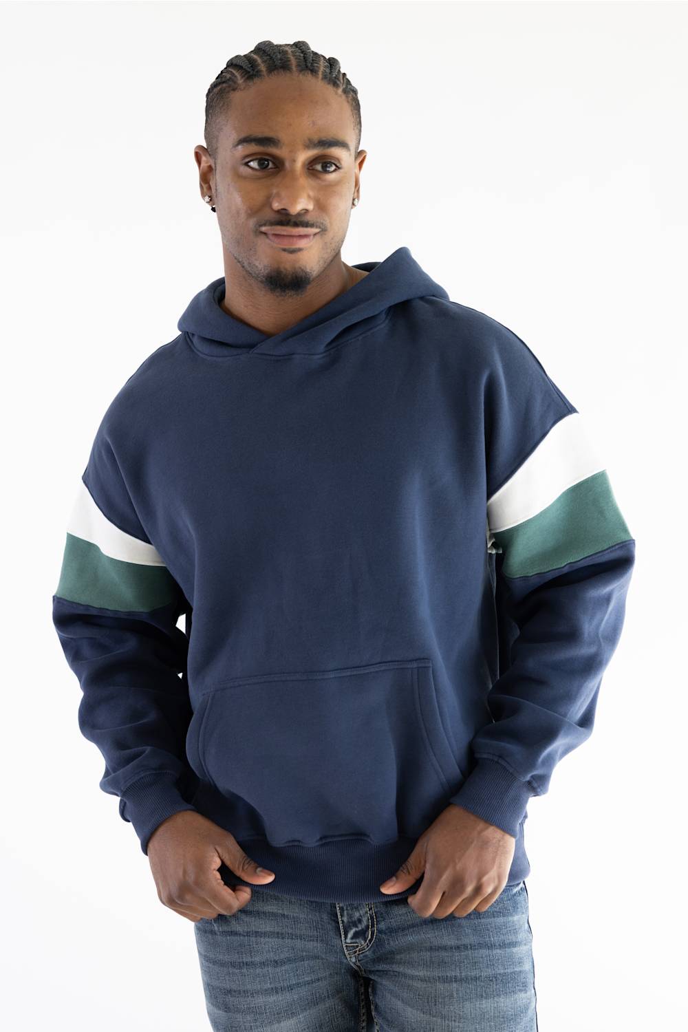 A man wearing a navy blue hoodie with white and green color-blocked stripes on the sleeves, paired with blue jeans, photographed against a plain white studio background.