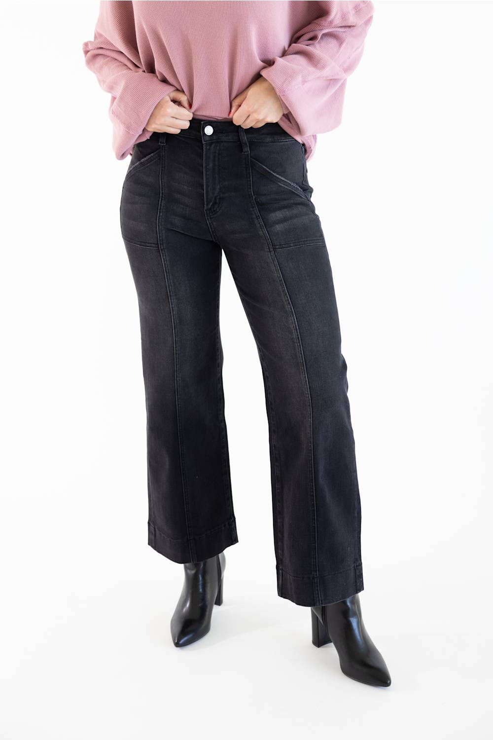 A model wearing black wide-leg cropped jeans, a dusty pink long-sleeve top, and black pointed-toe ankle boots, shown from the waist down against a plain white studio background.