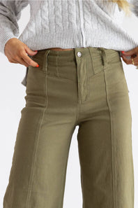A close-up of a person wearing olive green wide-leg pants with a gray cable-knit sweater, shown from the chest down against a light gray background.