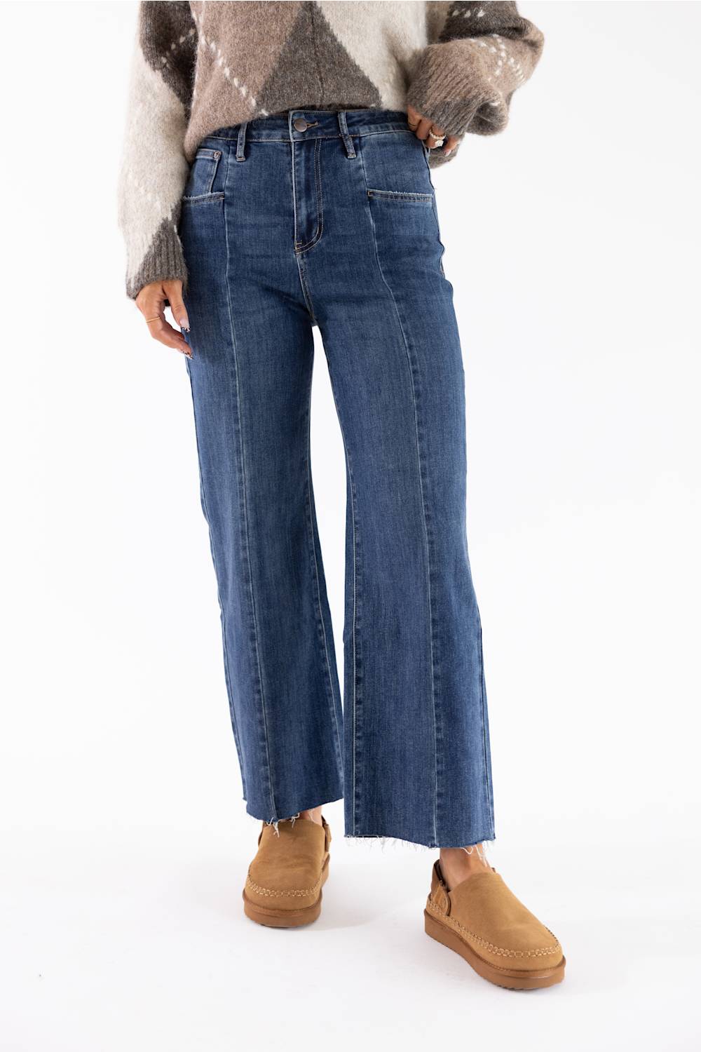 A person wearing blue wide-leg cropped jeans with a brown and beige knit sweater and tan slip-on shoes, shown from the chest down against a plain white studio background.