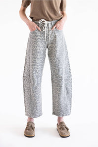 A person wearing loose, wide-leg cropped pants with a gray and white leopard print, paired with a brown top and brown slip-on shoes, photographed against a plain white studio background.