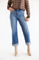 A model wearing a pair of medium-wash blue denim jeans with a straight-leg fit, cuffed hems, and subtle distressing, paired with a brown and beige striped sweater and beige ankle boots against a white studio background.