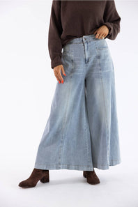A model wearing light-wash wide-leg denim jeans, a dark brown knit sweater, and brown suede ankle boots, standing against a plain white studio background.