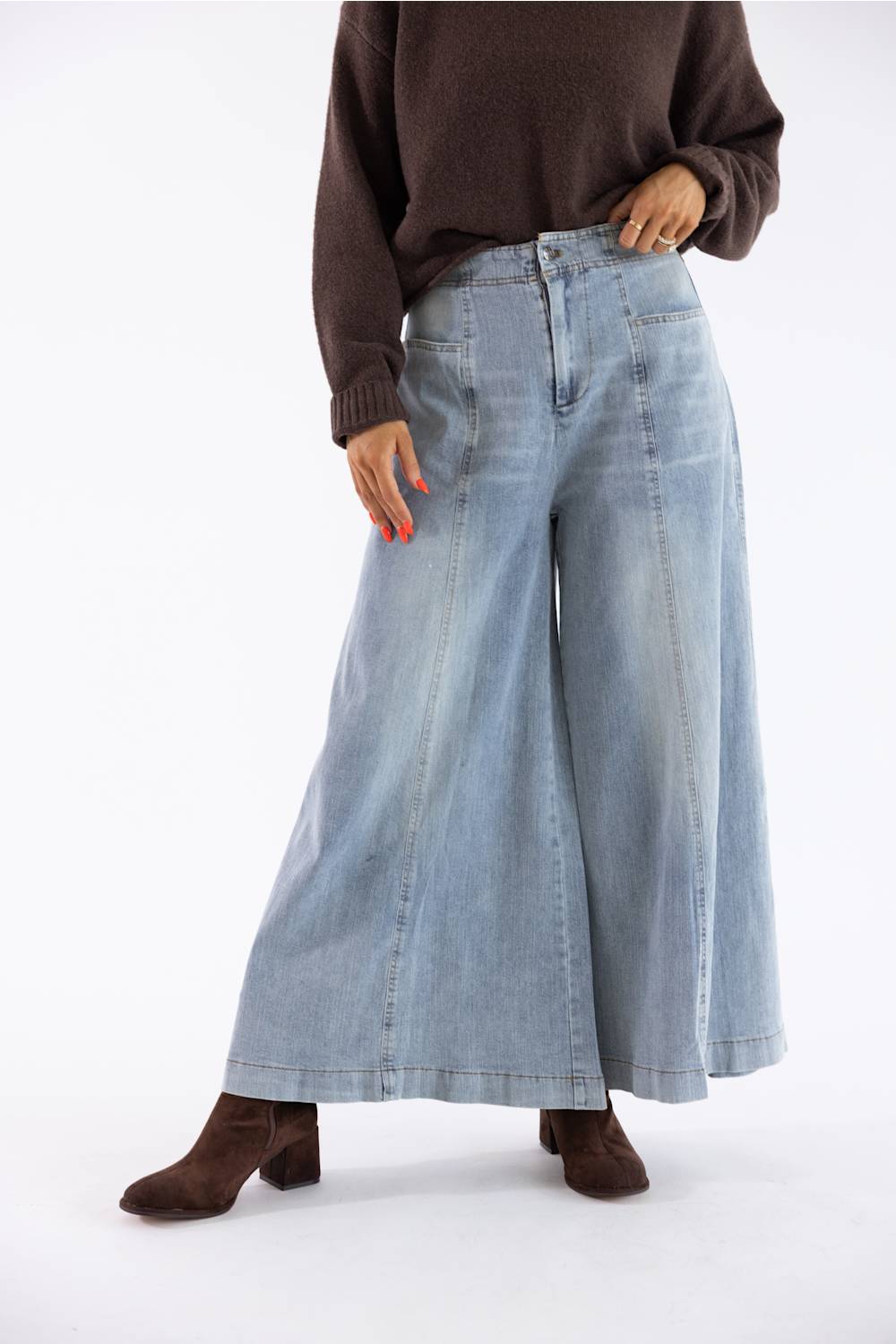A model wearing light-wash wide-leg denim jeans, a dark brown knit sweater, and brown suede ankle boots, standing against a plain white studio background.