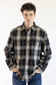 A man wearing a long-sleeve Carhartt plaid button-up shirt in black, gray, and white with thin orange stripes, paired with blue jeans, against a plain white background.
