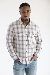 Front view of a man wearing the Hallstatt Knit Button Up Flannel Shirt in Sand with a plaid pattern in blue, beige, and gray, paired with light-wash jeans against a white backdrop.