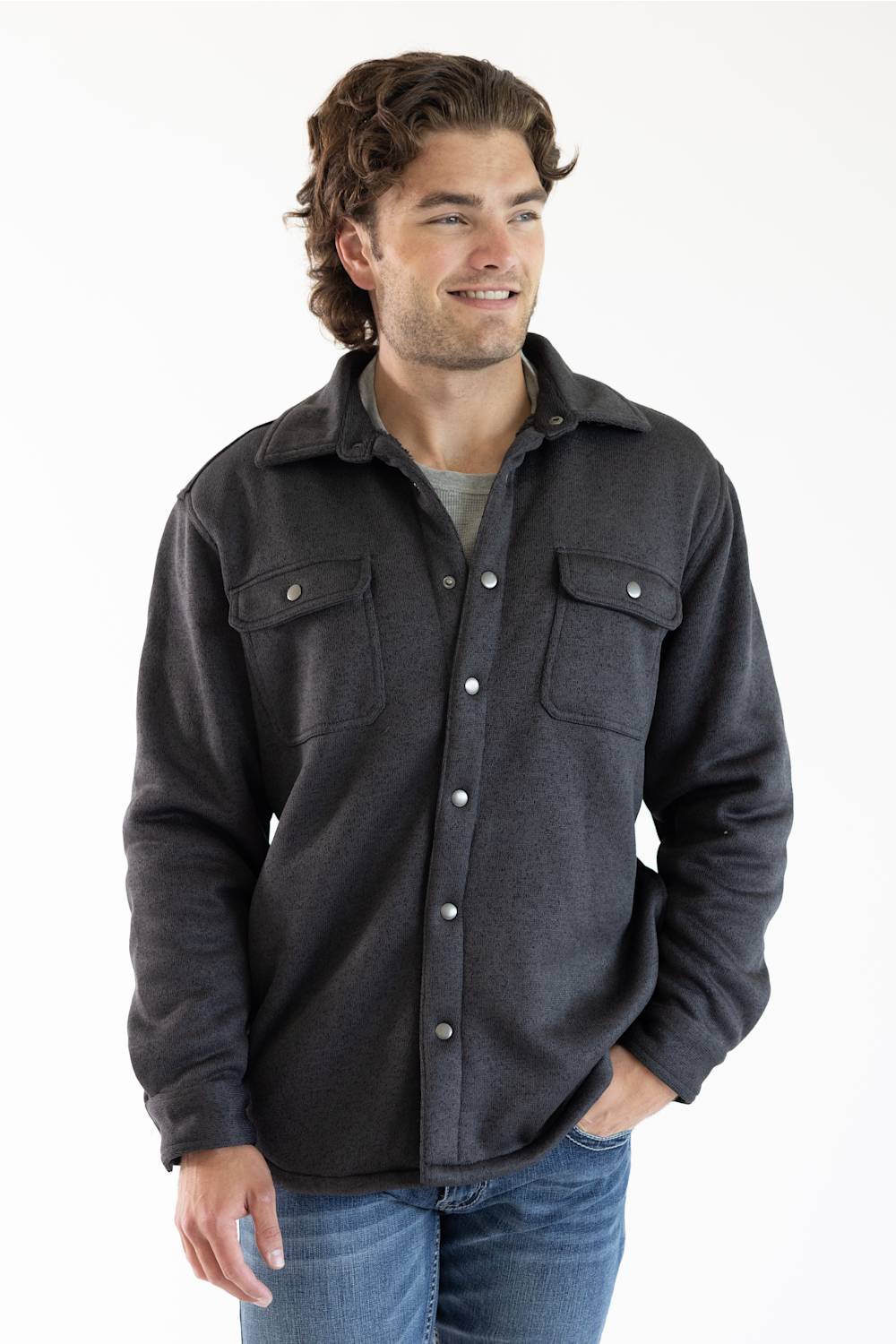 A man wearing a dark charcoal gray button-up flannel shirt jacket with two chest pockets and silver snap buttons, paired with blue jeans.