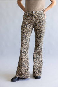A person wearing leopard-print flare pants with a beige top and black shoes, standing against a light gray studio background.