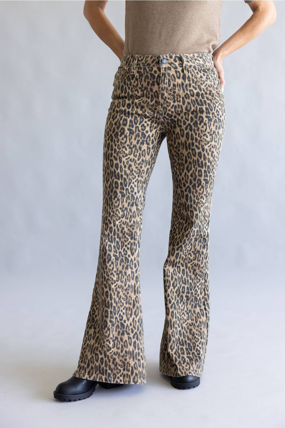 A person wearing leopard-print flare pants with a beige top and black shoes, standing against a light gray studio background.