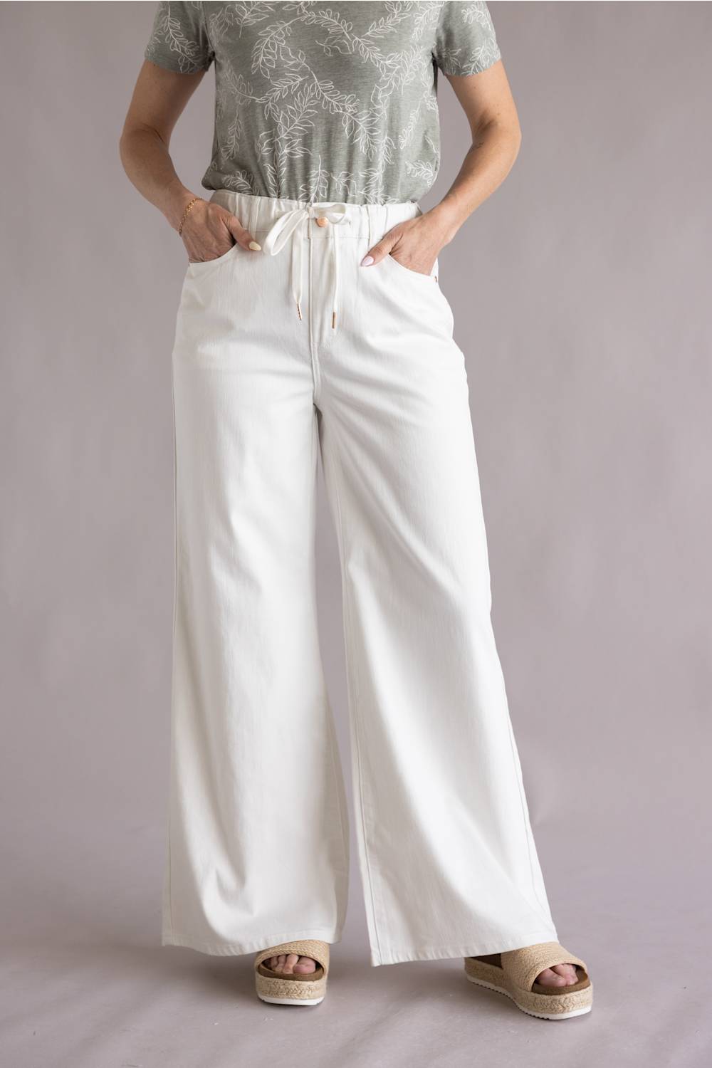 Judy Blue White Featherweight Palazzo Jeans for Women in White; Person wearing a green patterned top and white wide-leg pants on a plain background