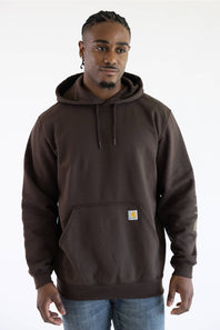 Front-facing view from the waist up of a male model against a plain white background, wearing a dark clove brown Carhartt hooded sweatshirt with a small chest logo patch and drawstring hood, paired with medium wash denim jeans.