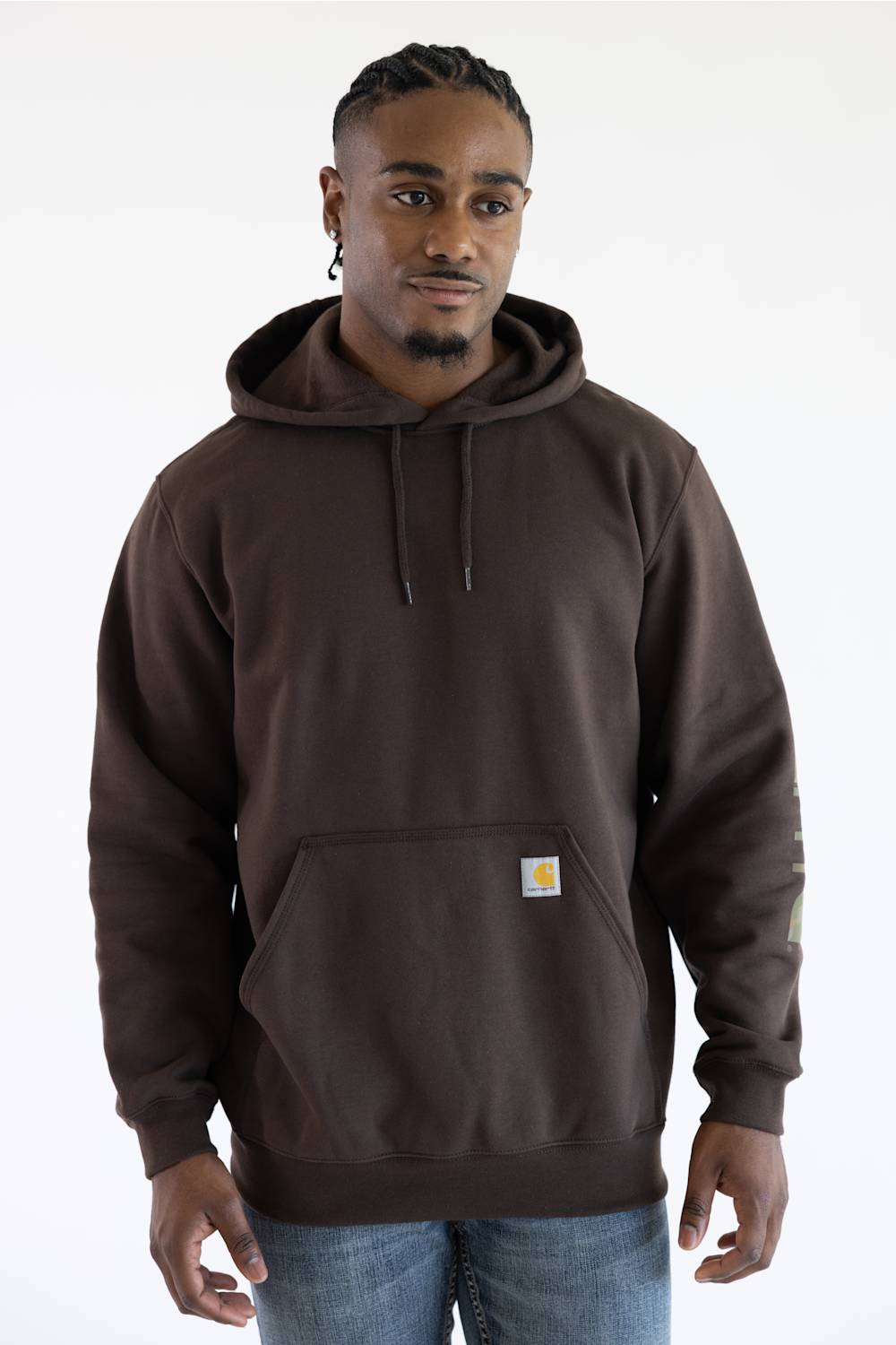 Front-facing view from the waist up of a male model against a plain white background, wearing a dark clove brown Carhartt hooded sweatshirt with a small chest logo patch and drawstring hood, paired with medium wash denim jeans.