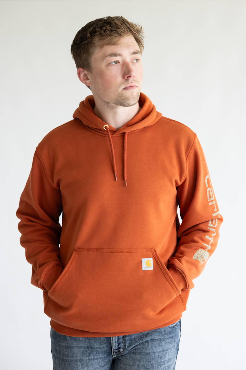 Man wearing a burnt orange colored hoodie, with Carhartt logo down the left arm sleeve. 
