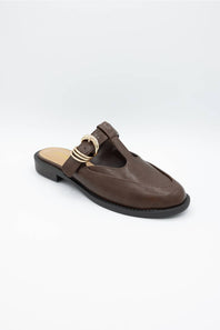 A dark brown leather mule sandal with a decorative gold-tone buckle detail on the strap, shown against a plain light gray background.