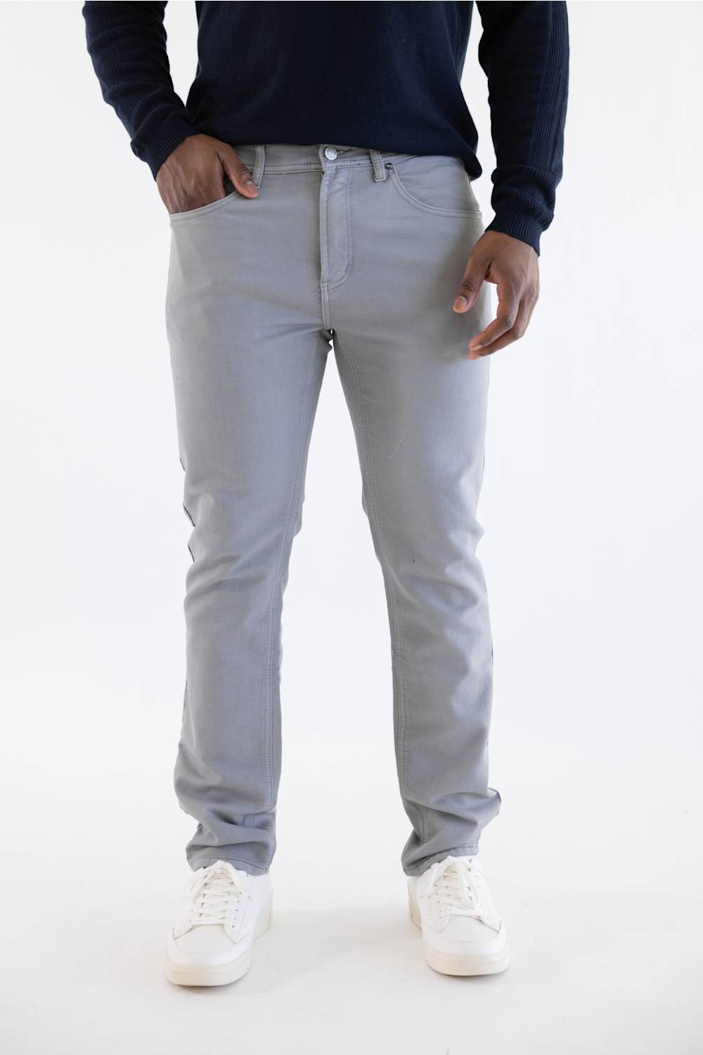 A person wearing light gray slim-fit jeans, a dark navy long-sleeve top, and white sneakers, standing against a plain white studio background.
