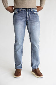 A person wearing light-wash blue denim jeans with a beige knit sweater and brown shoes, shown from the waist down against a plain light background.