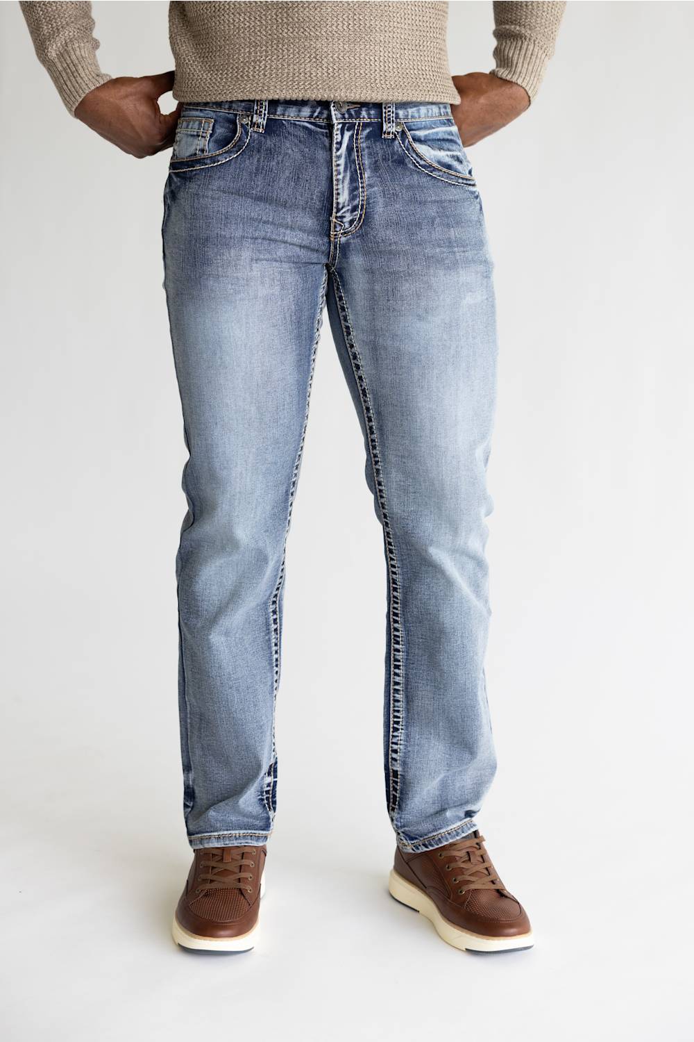 A person wearing light-wash blue denim jeans with a beige knit sweater and brown shoes, shown from the waist down against a plain light background.