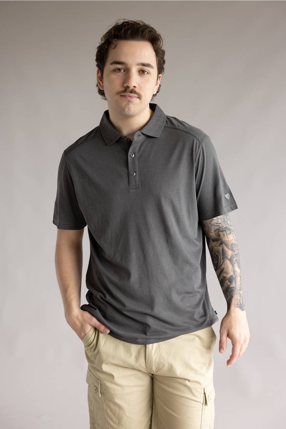 Kuhl De Facto Polo Shirt for Men in Carbon; Man wearing a gray polo shirt and beige pants against a plain background