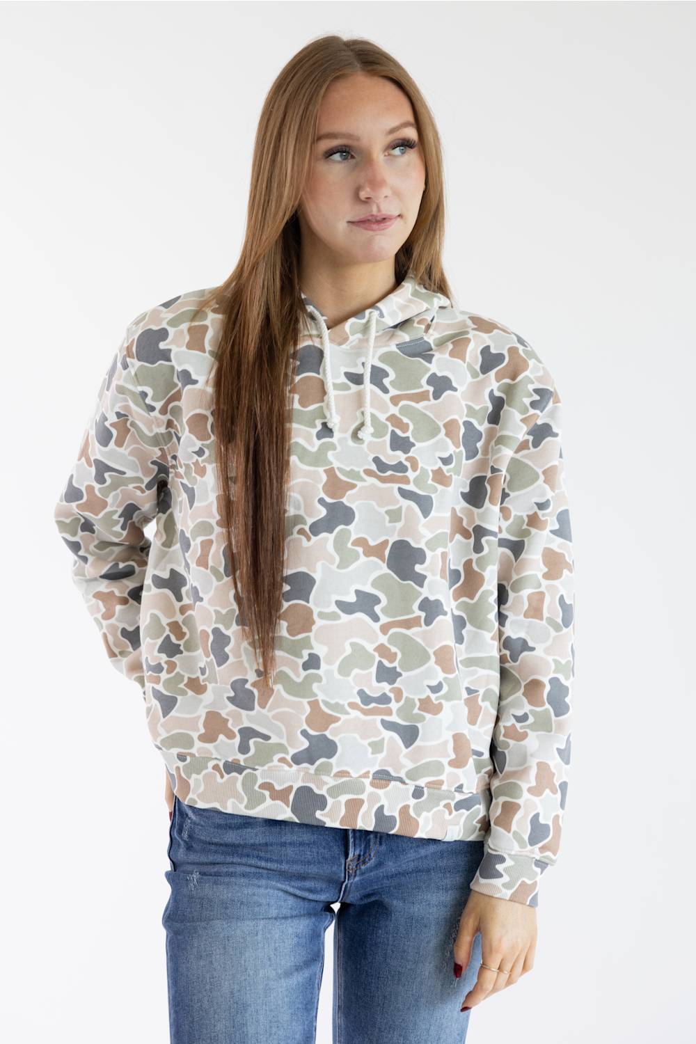 A woman modeling a camouflage-patterned hoodie with blue jeans against a plain white studio background.