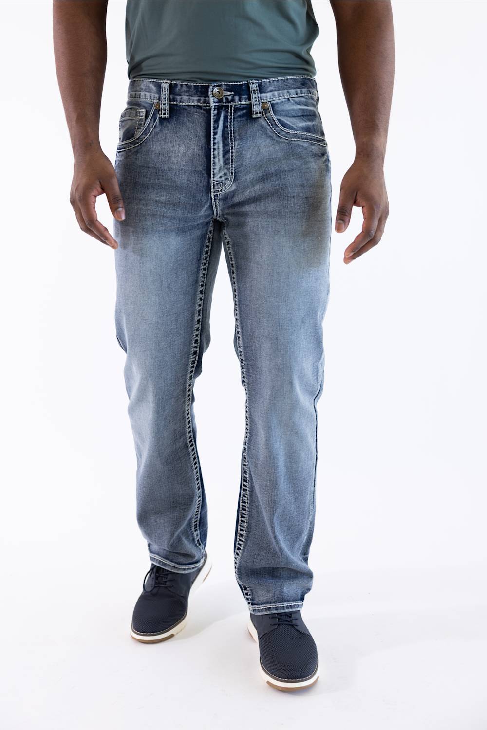 A person wearing light blue denim jeans with a faded wash, paired with a dark green shirt and dark navy shoes, shown from the waist down against a plain white studio background.