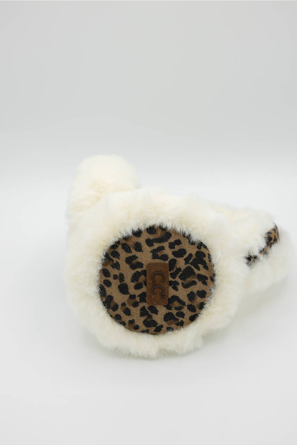 White faux fur slippers with a leopard print circular patch on the sole, featuring a small brown brand tab in the center.