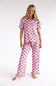 A woman modeling a two-piece pink pajama set with a red bow pattern, consisting of a short-sleeve top and matching pants, against a plain white studio background.