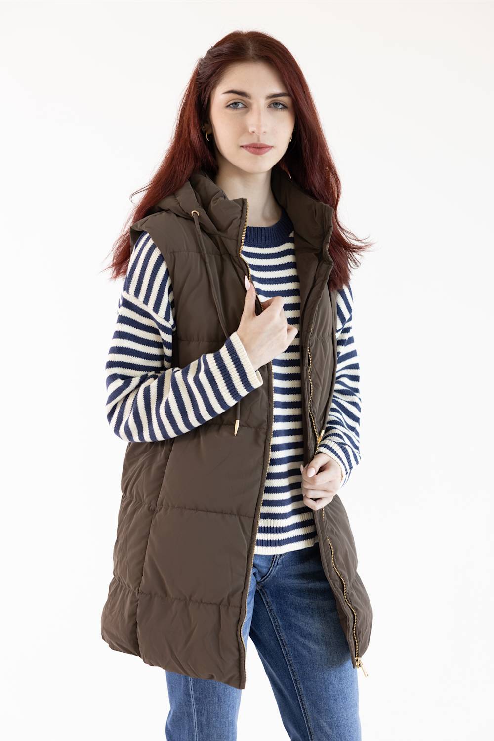 A woman with red hair wearing a brown sleeveless puffer vest over a navy and white striped long-sleeve shirt, paired with blue jeans, against a plain white background.