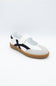 A white slip-on shoe with a black side stripe and a brown gum sole, photographed on a light gray background.