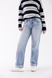 A model wearing light-wash blue straight-leg jeans, a navy and white striped sweater, and white sneakers, shown from the chest down against a plain white studio background.