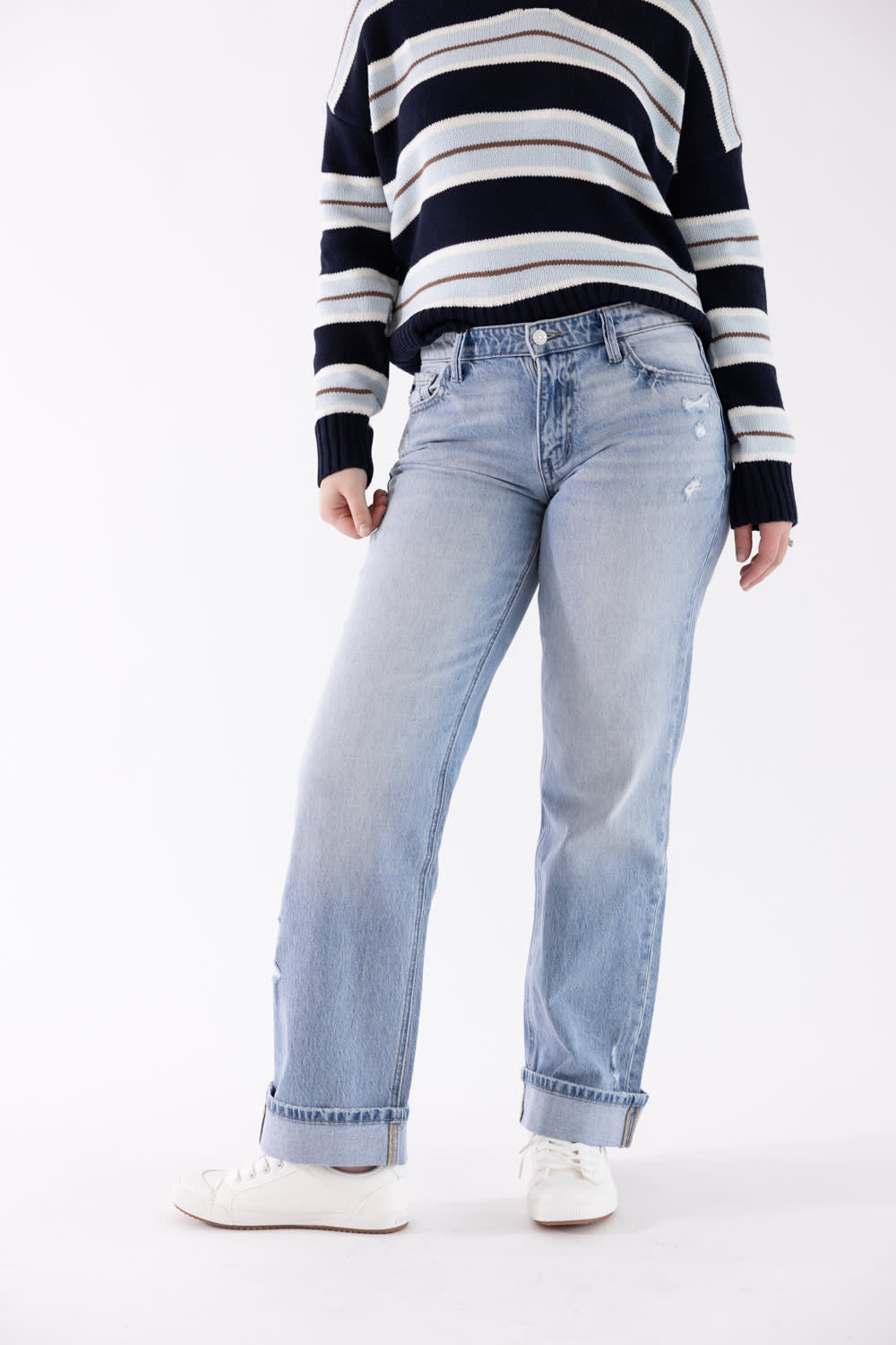 A model wearing light-wash blue straight-leg jeans, a navy and white striped sweater, and white sneakers, shown from the chest down against a plain white studio background.