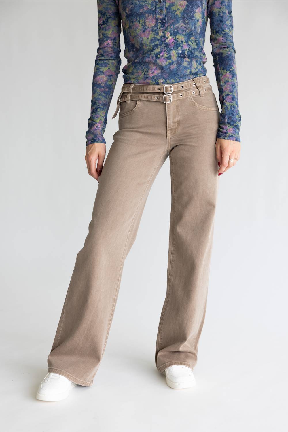 A model wearing beige wide-leg corduroy pants with a matching belt, styled with a floral long-sleeve top and white sneakers against a light gray background.