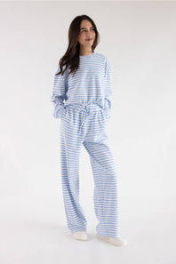A woman modeling a matching light blue and white striped lounge set, consisting of a long-sleeve top and wide-leg pants, against a plain white studio background.